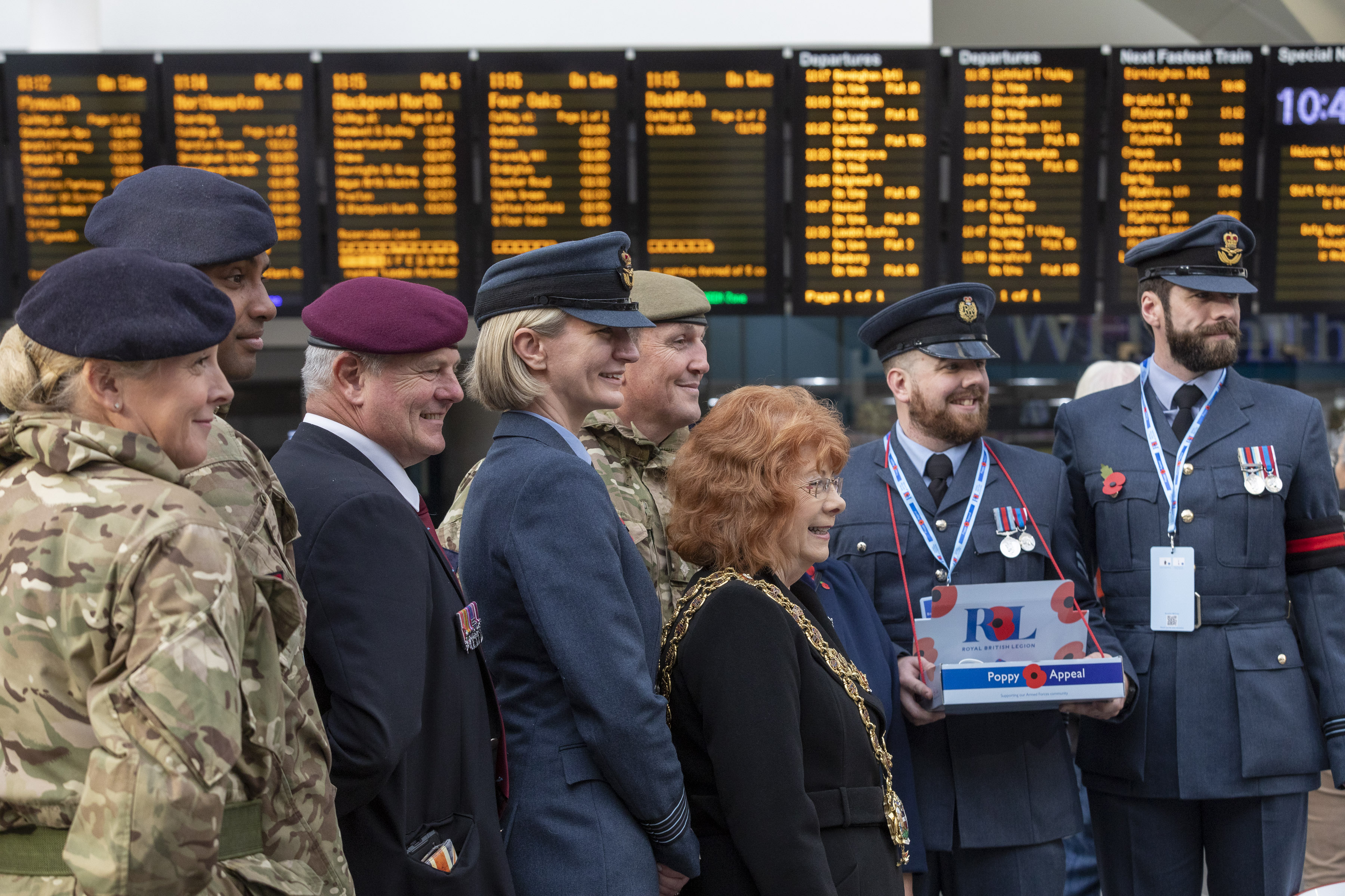Image shows RAF aviators holding poppy collection boxes in train station.
